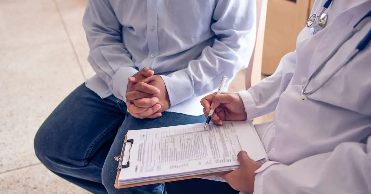 a doctor sitting beside a patient, filling out a medical form