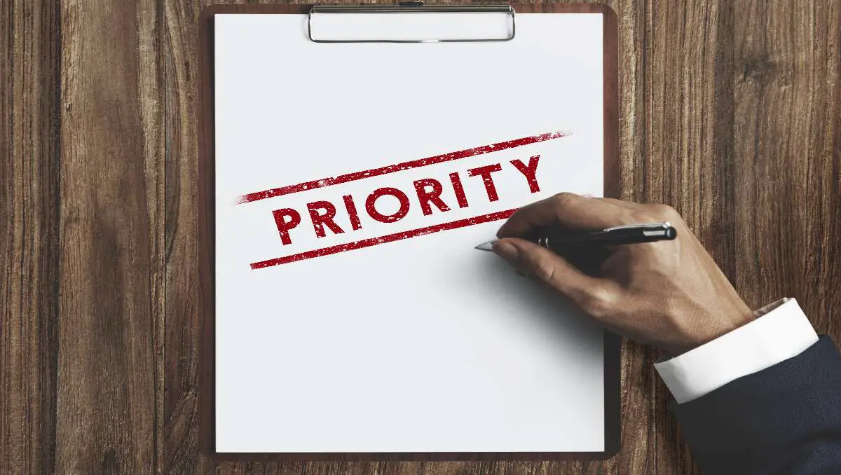 A hand writing a big "priority" word on the paper using a red ink.