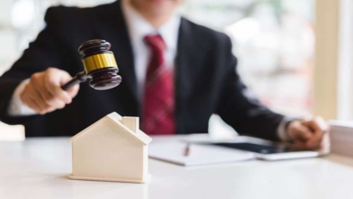 A housing authority employee holding a gavel on top of a miniature model house.